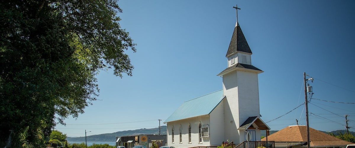 Una iglesia con campanario y cartel, una carretera con coches, y un cielo azul despejado.