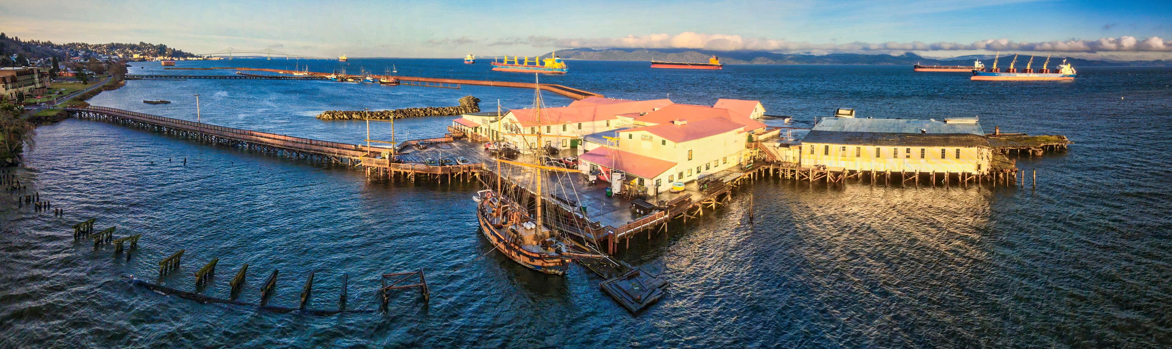 A harbor with a prominent pier, a large ship, and a bridge in the background.