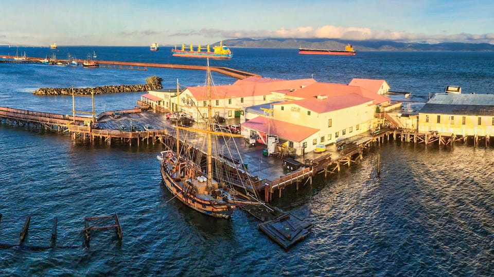 A harbor with a prominent pier, a large ship, and a bridge in the background.
