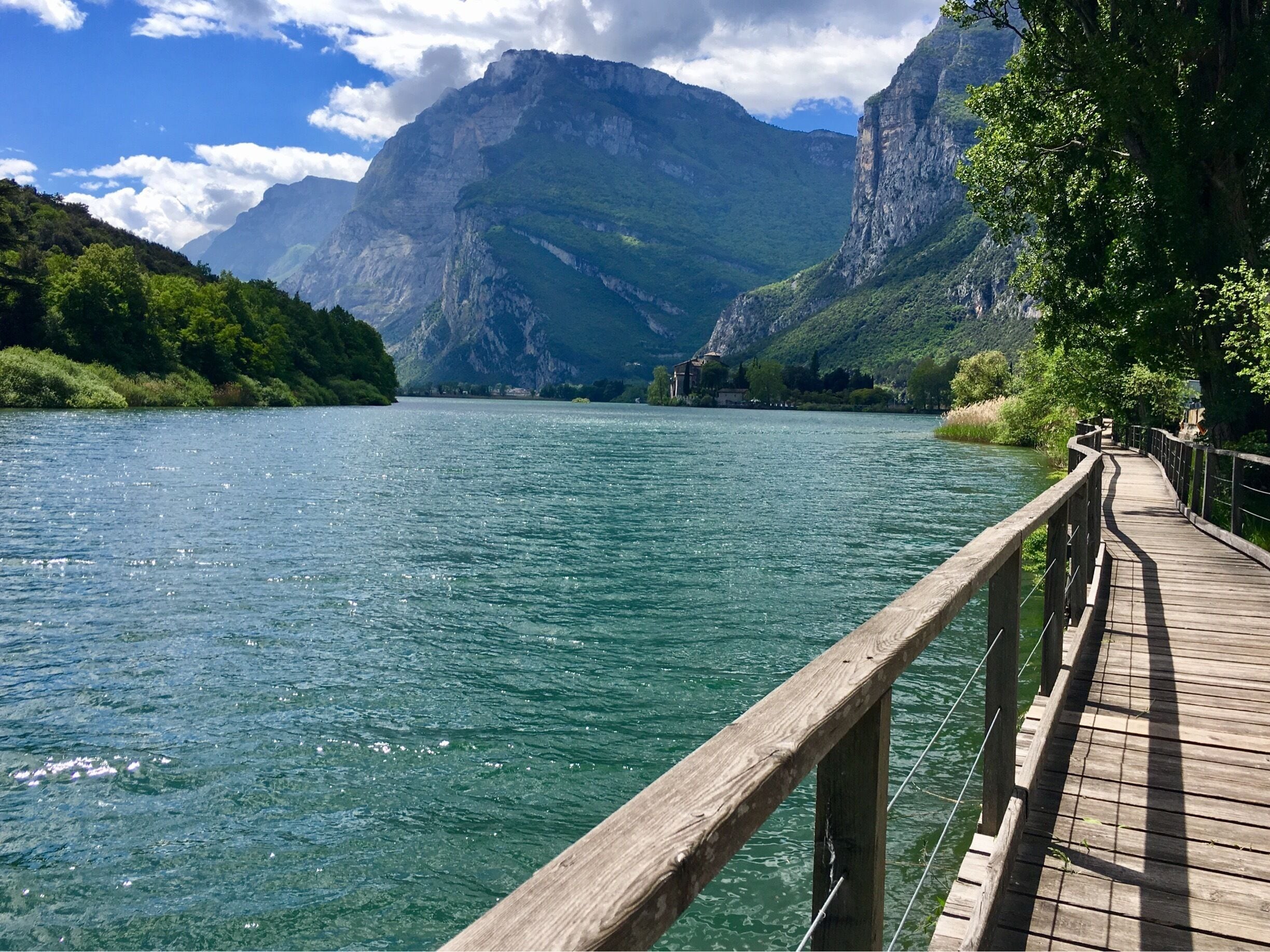 A wooden boardwalk along a clear lake with mountains in the background.