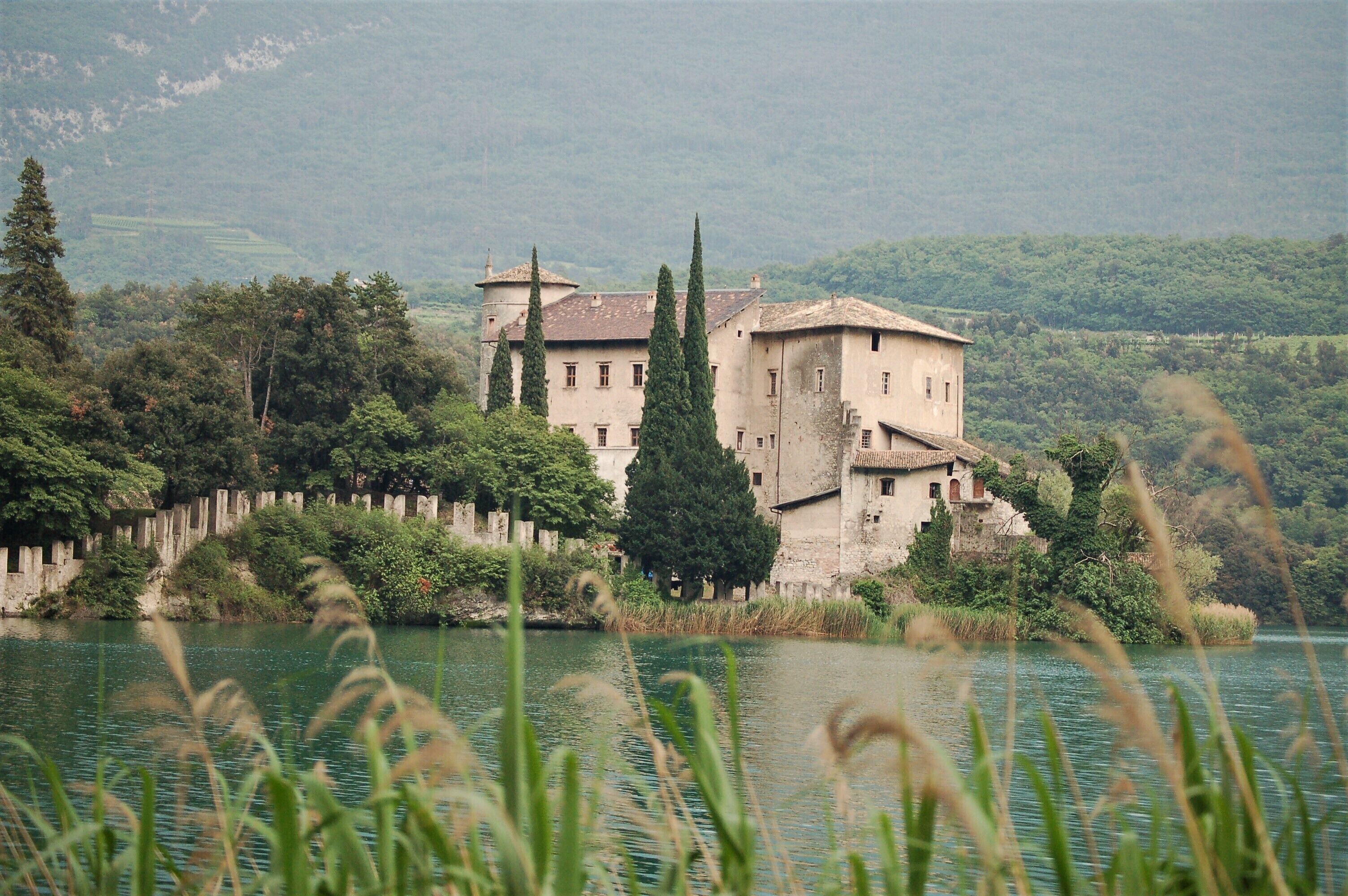 Um edifício histórico rodeado por um lago e colinas florestadas.