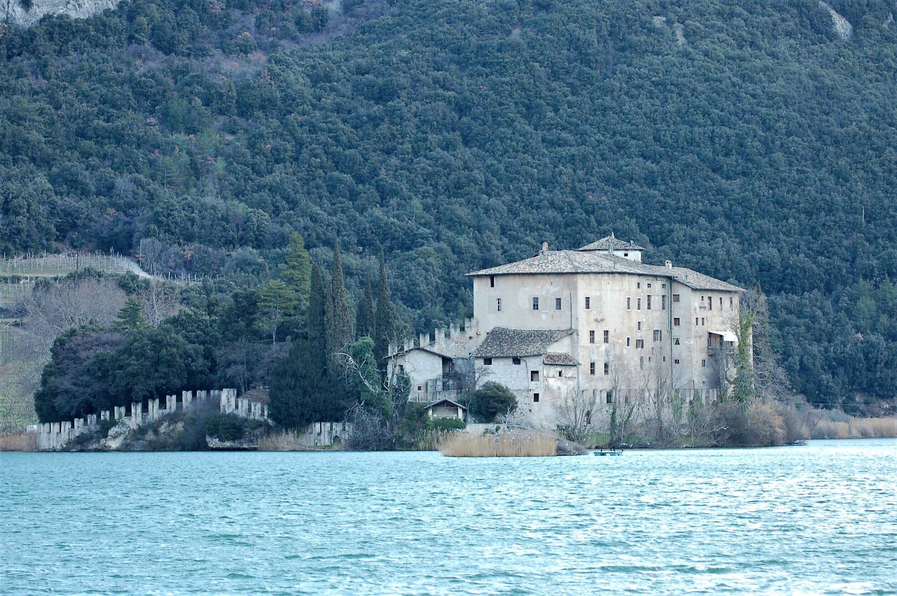 Un edificio grande e histórico rodeado de agua y un bosque frondoso.