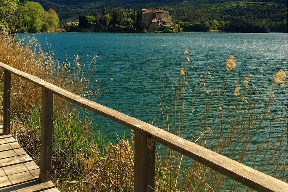 Um calçadão de madeira que leva a um lago, com uma casa numa colina ao fundo.