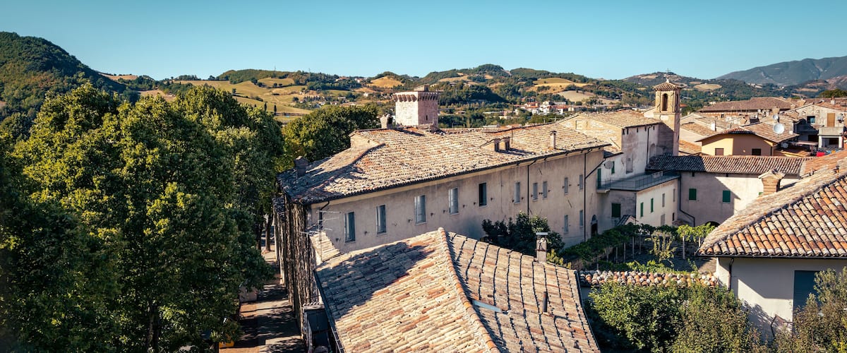 A village with terracotta-roofed buildings, lush green hills, and a clear blue sky.