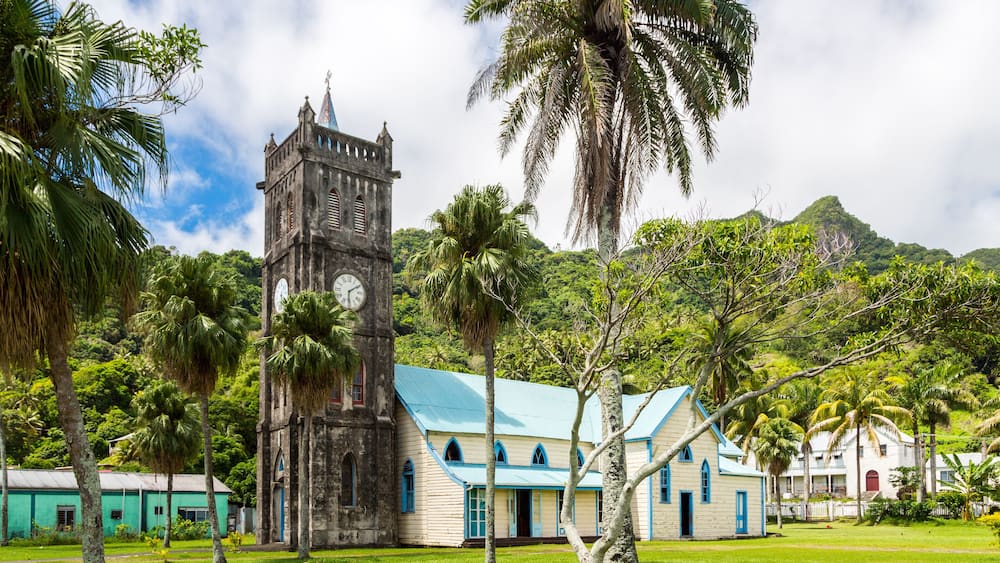 A historic church with a clock tower, a small chapel, and lush greenery.