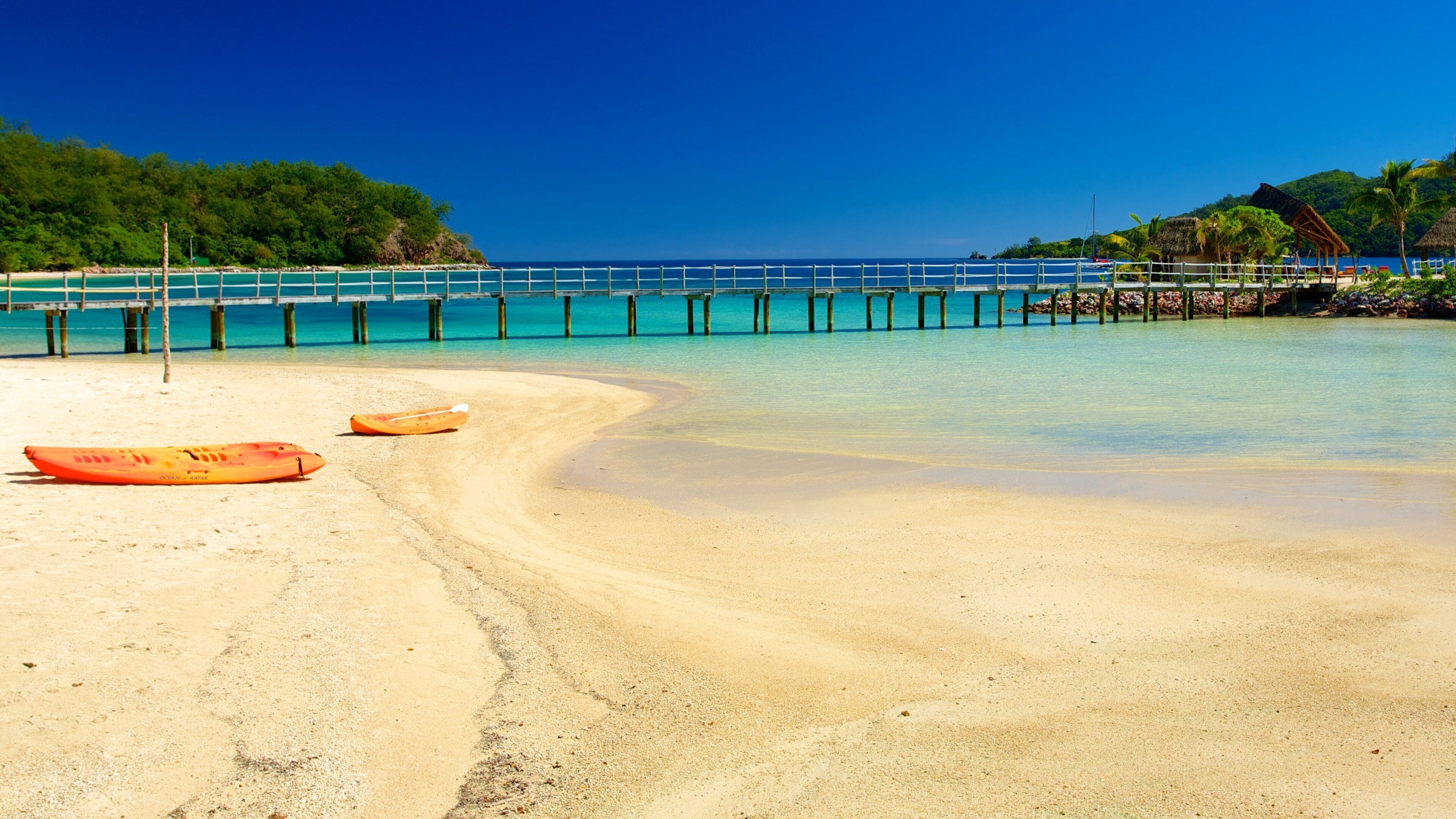A beach with two kayaks, a wooden pier, and a thatched-roof hut.