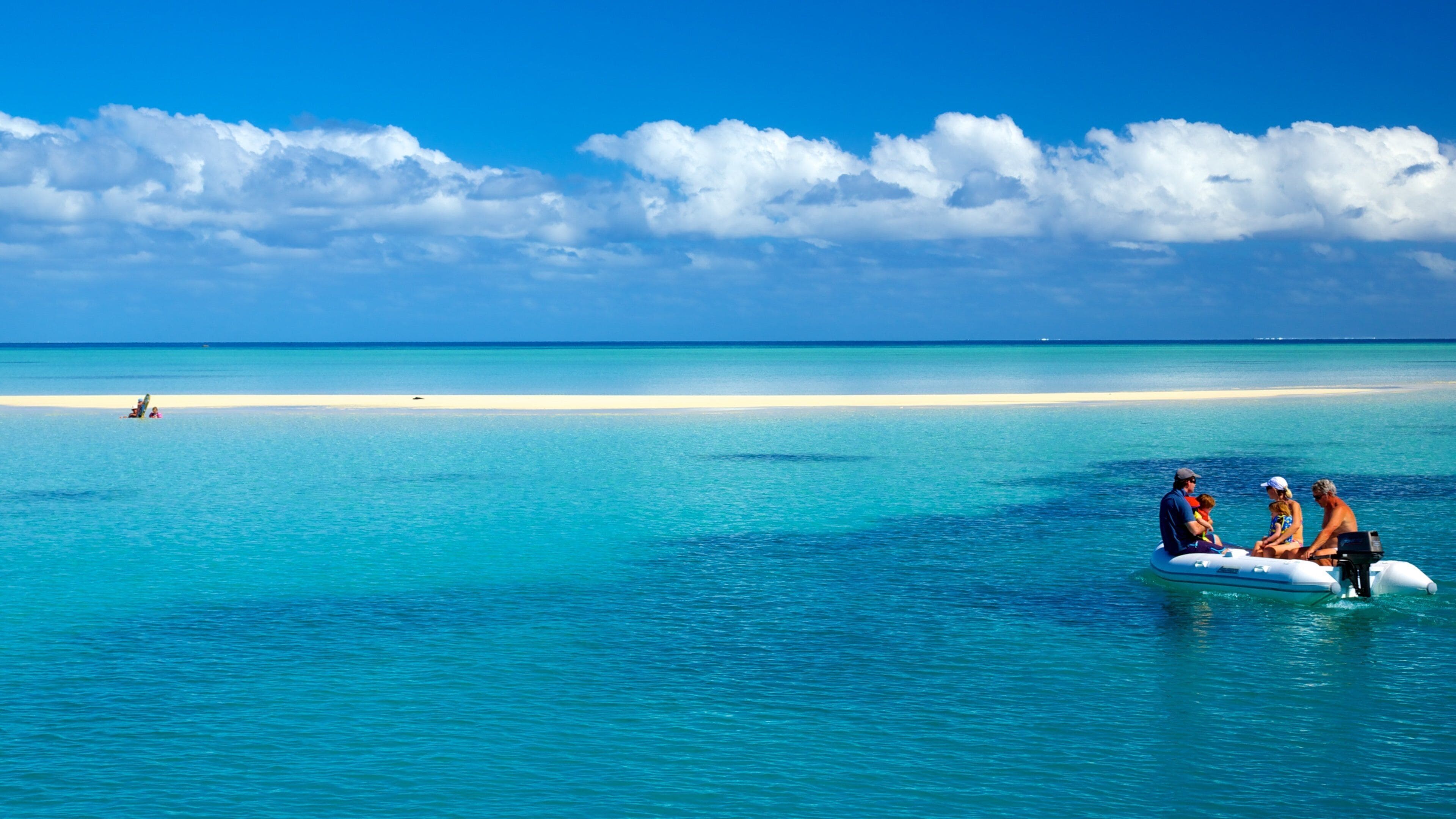 A clear blue sea with a sandy beach and a few people on a boat.