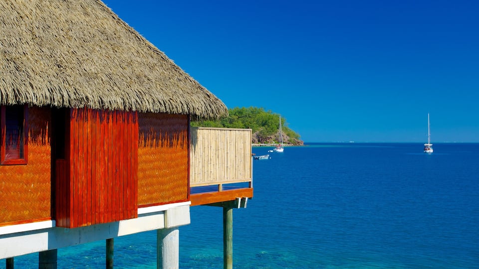 A thatched-roof house with a wooden deck extending over turquoise water.