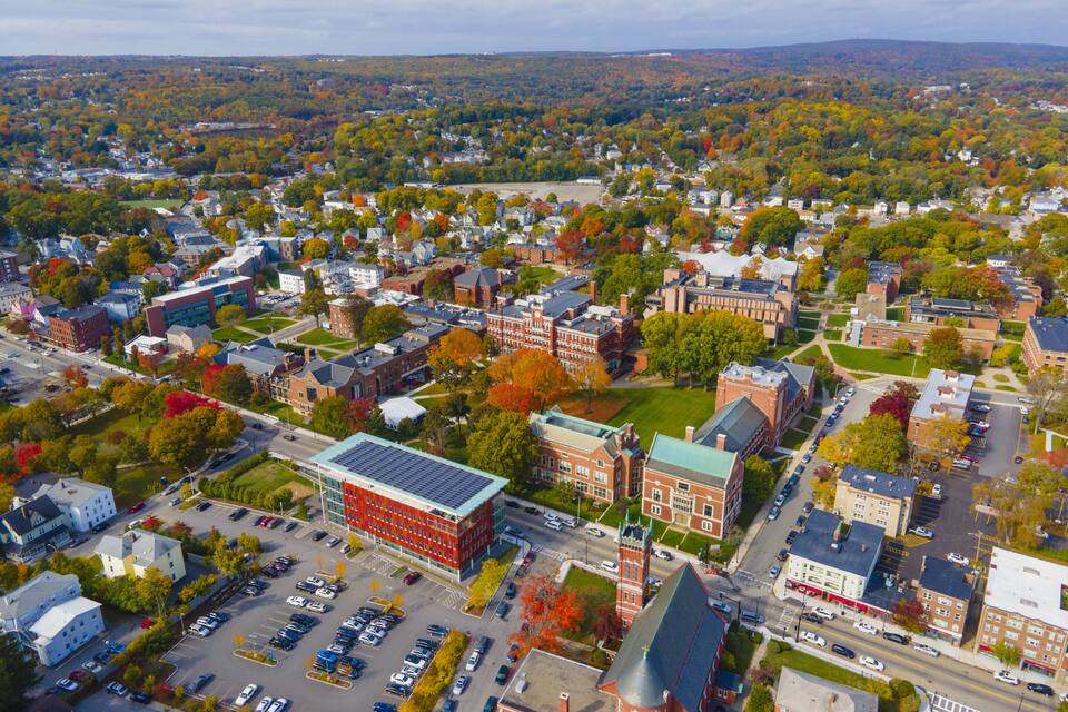 An aerial view of a town with autumn foliage, a prominent red building with a green roof, and a parking lot.