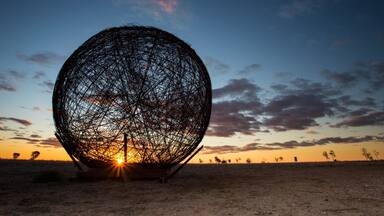 A large spherical structure in a desert landscape at sunset.