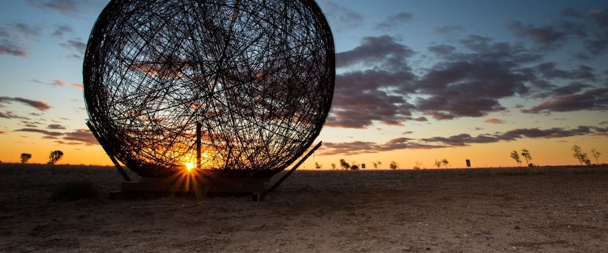 A large spherical structure in a desert landscape at sunset.