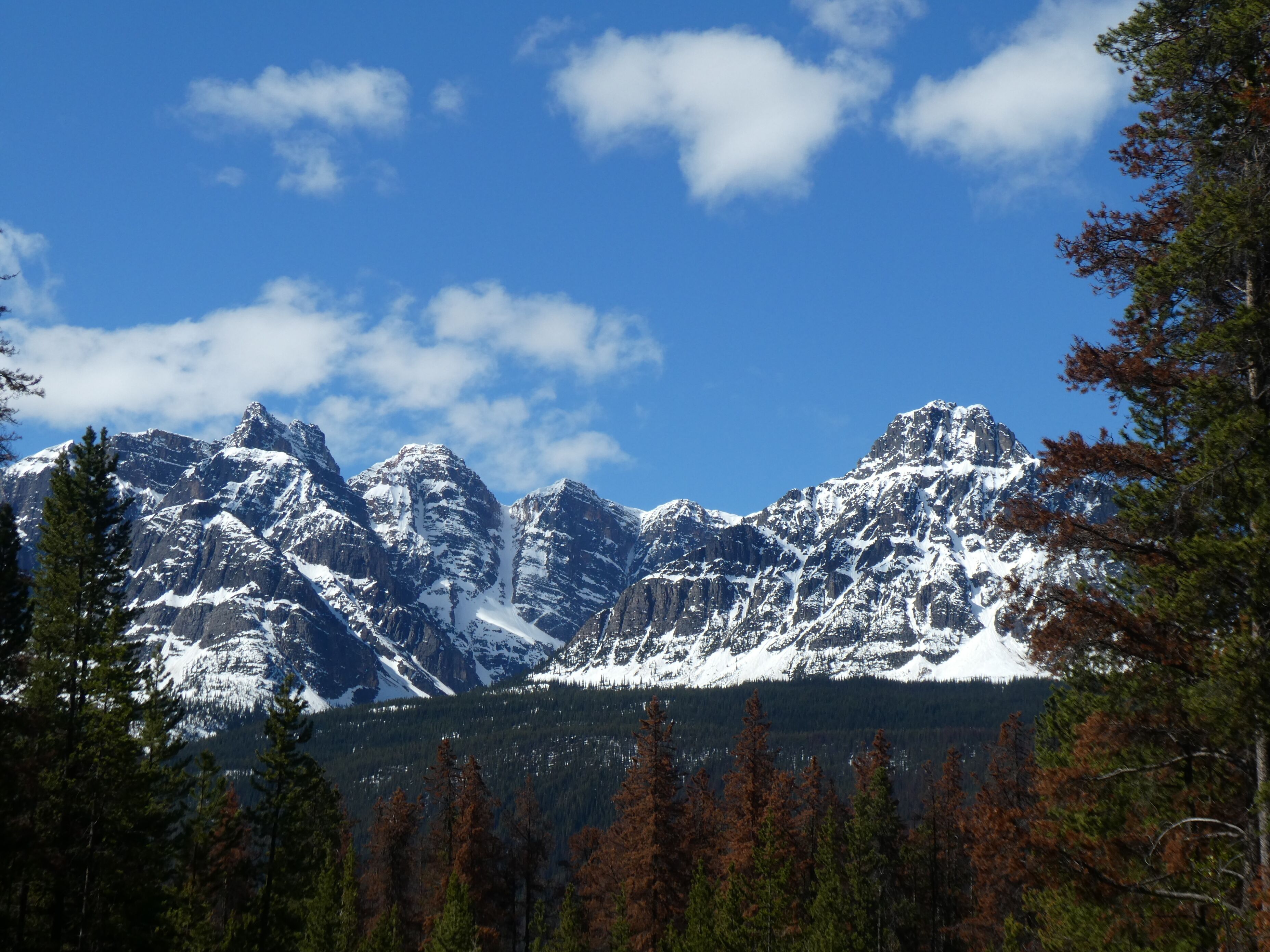 A snow-covered mountain range with a clear blue sky and scattered clouds.
