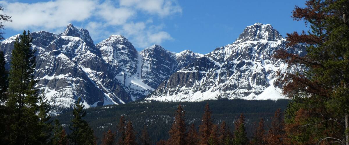 A snow-covered mountain range with a clear blue sky and scattered clouds.