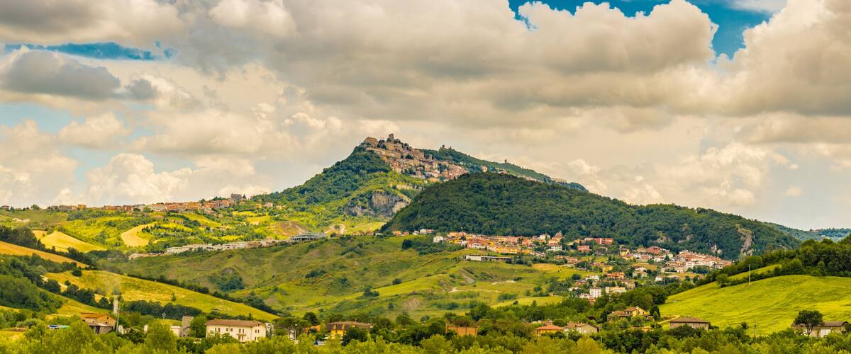 A mountainous landscape with a castle on top, surrounded by green fields and a small village.