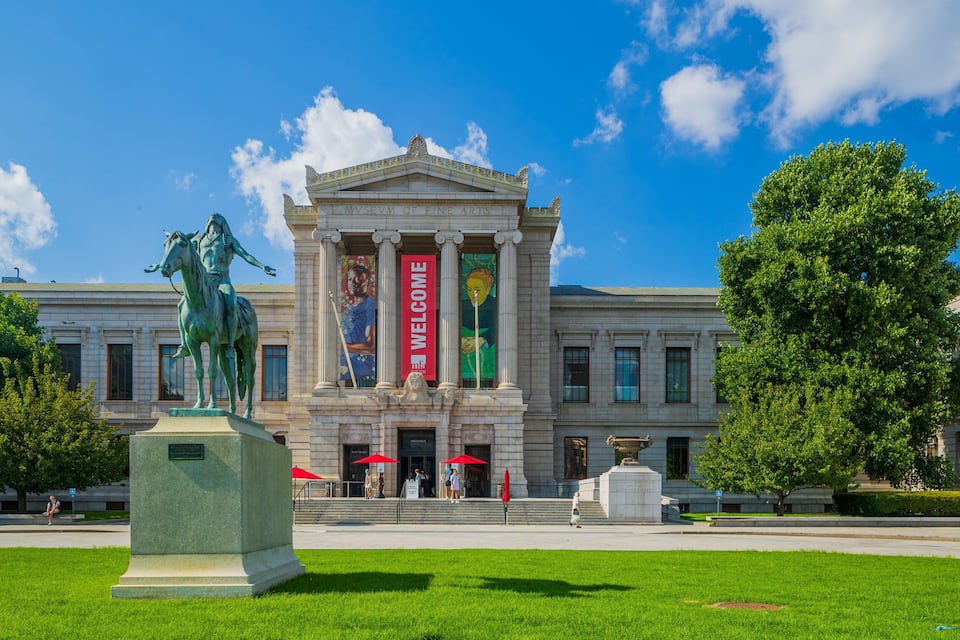 The Museum of Fine Arts with a large equestrian statue in front, a 'Welcome' banner, and a clear blue sky.