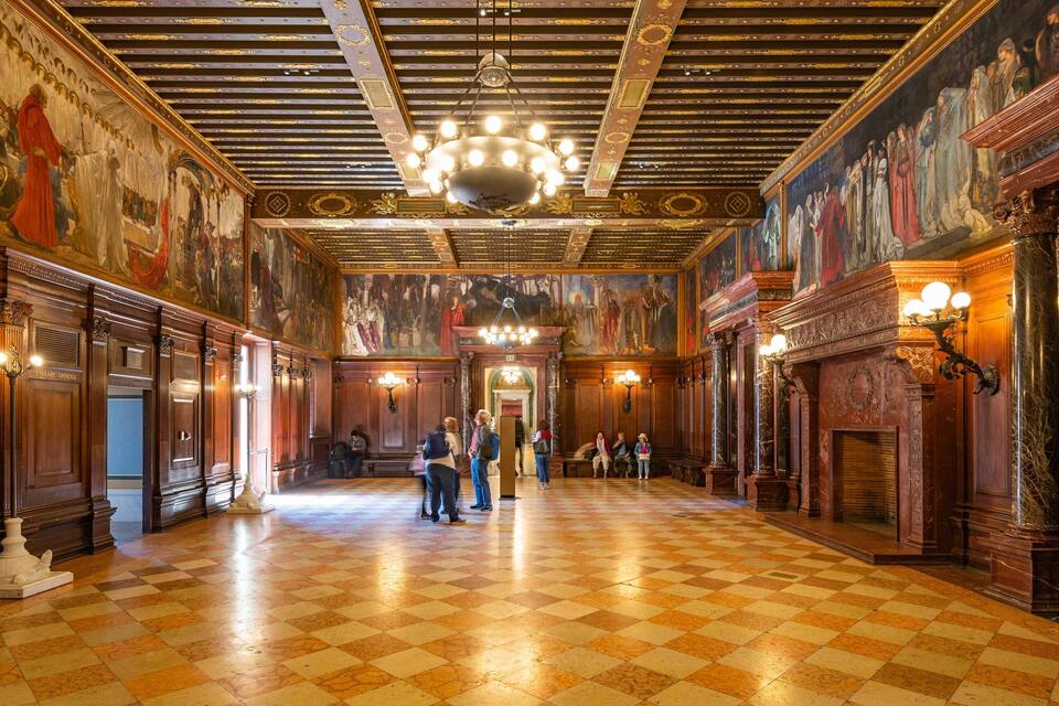Un salón imponente con paneles de madera decorados, suelo a cuadros y una gran lámpara de araña.