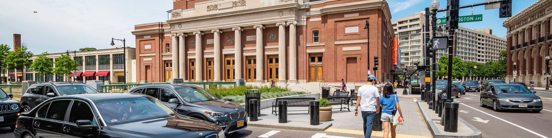 A black BMW at a crosswalk in front of a large brick building with columns and a clock.