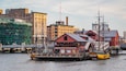 A historic waterfront with a tall ship docked at a pier, surrounded by industrial buildings and a bridge.