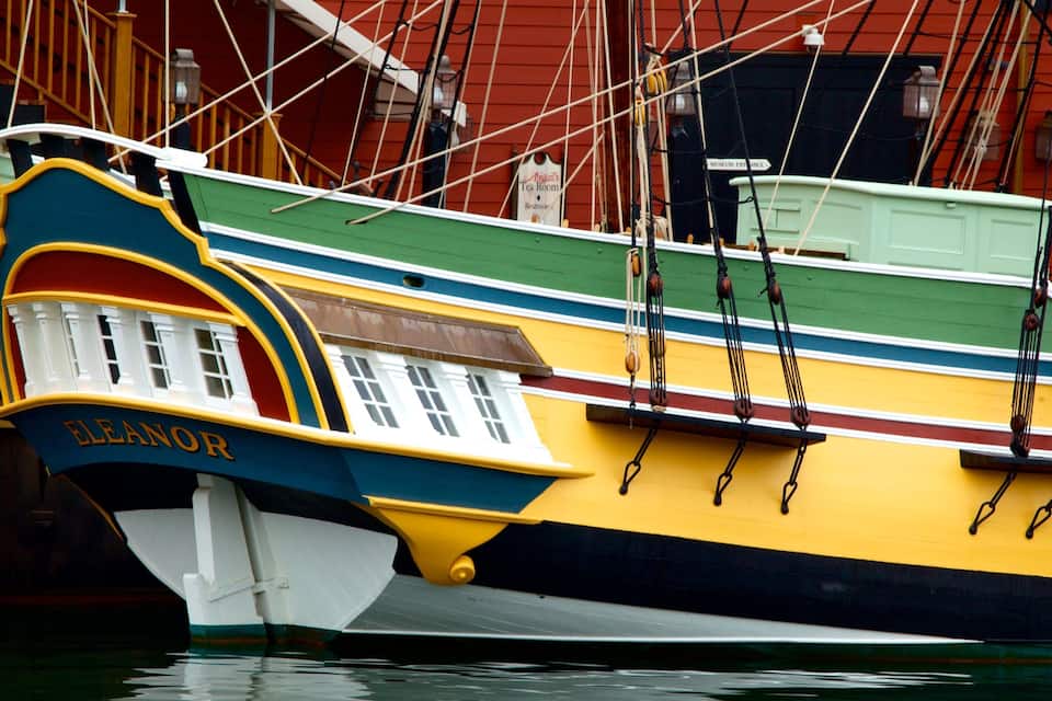 Un bote colorido llamado 'ELEANOR' amarrado en un muelle, con un edificio rojo al fondo.