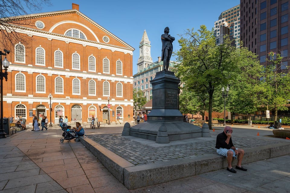 A public square with a statue, a red brick building, and modern high-rise buildings.