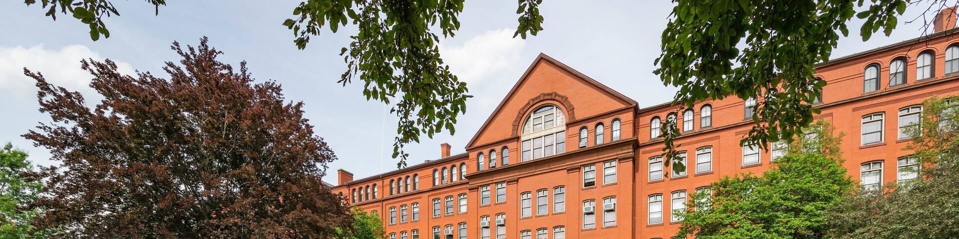 A red brick building with arched windows and a central entrance, surrounded by green lawns and trees.
