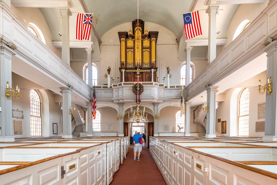 A church interior with rows of pews, a large organ, and American flags.