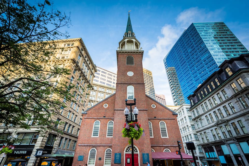 A historic church with a tall steeple, surrounded by modern skyscrapers and older buildings.
