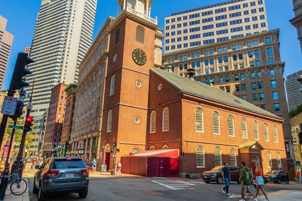 A historic building with a clock tower, surrounded by modern skyscrapers.