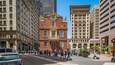 A busy urban street with historic buildings, pedestrians, and modern high-rises.