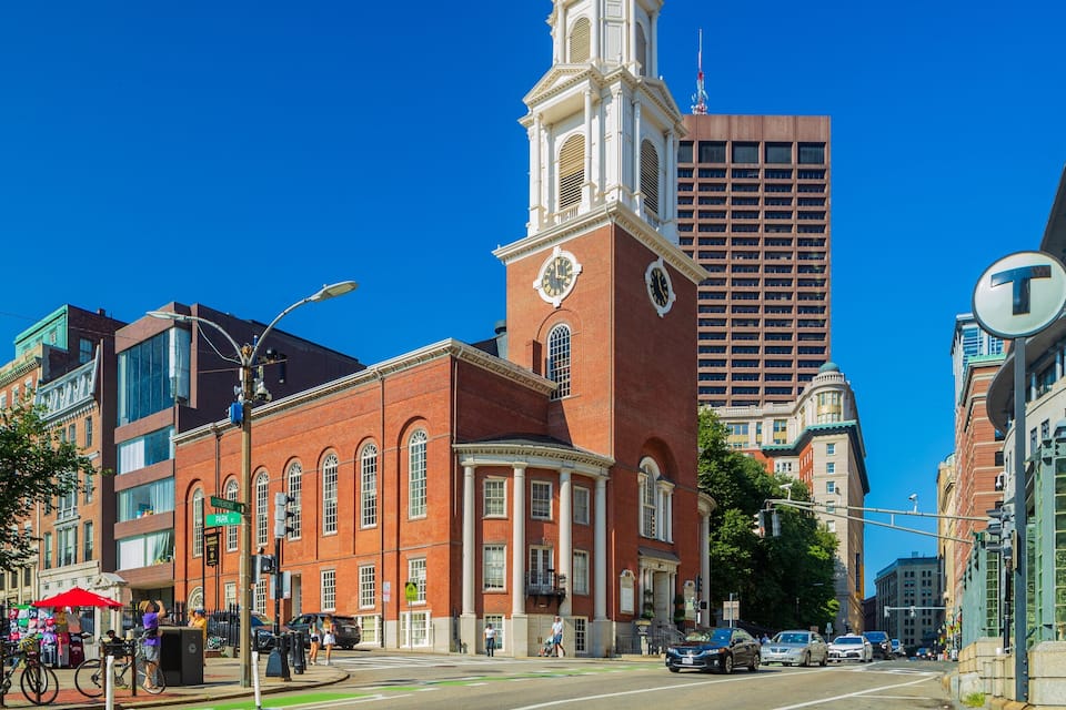 A historic building with a clock tower, a modern high-rise, and a street with pedestrians and cars.