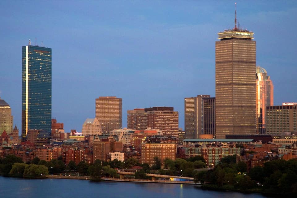 A city skyline with modern skyscrapers and a river in the foreground.