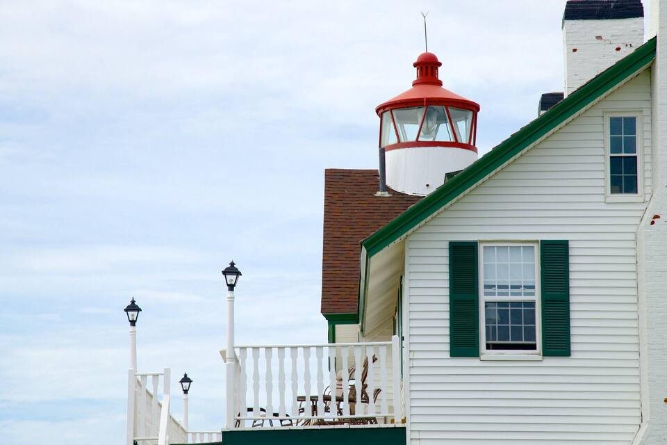 A white building with green shutters and a red and white lighthouse.