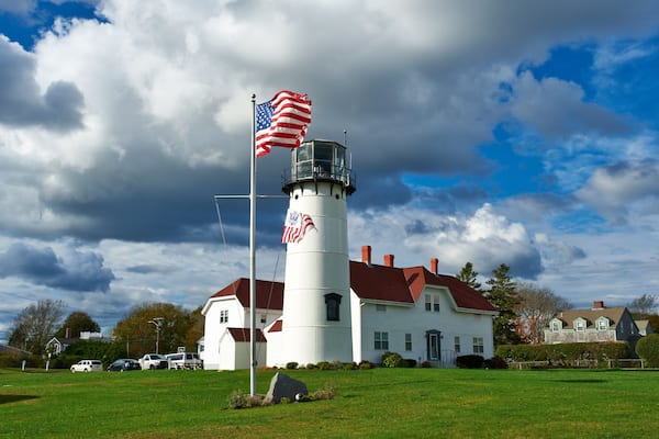 Et fyrtårn med et amerikansk flag, en hvid bygning med rødt tag og en overskyet himmel.