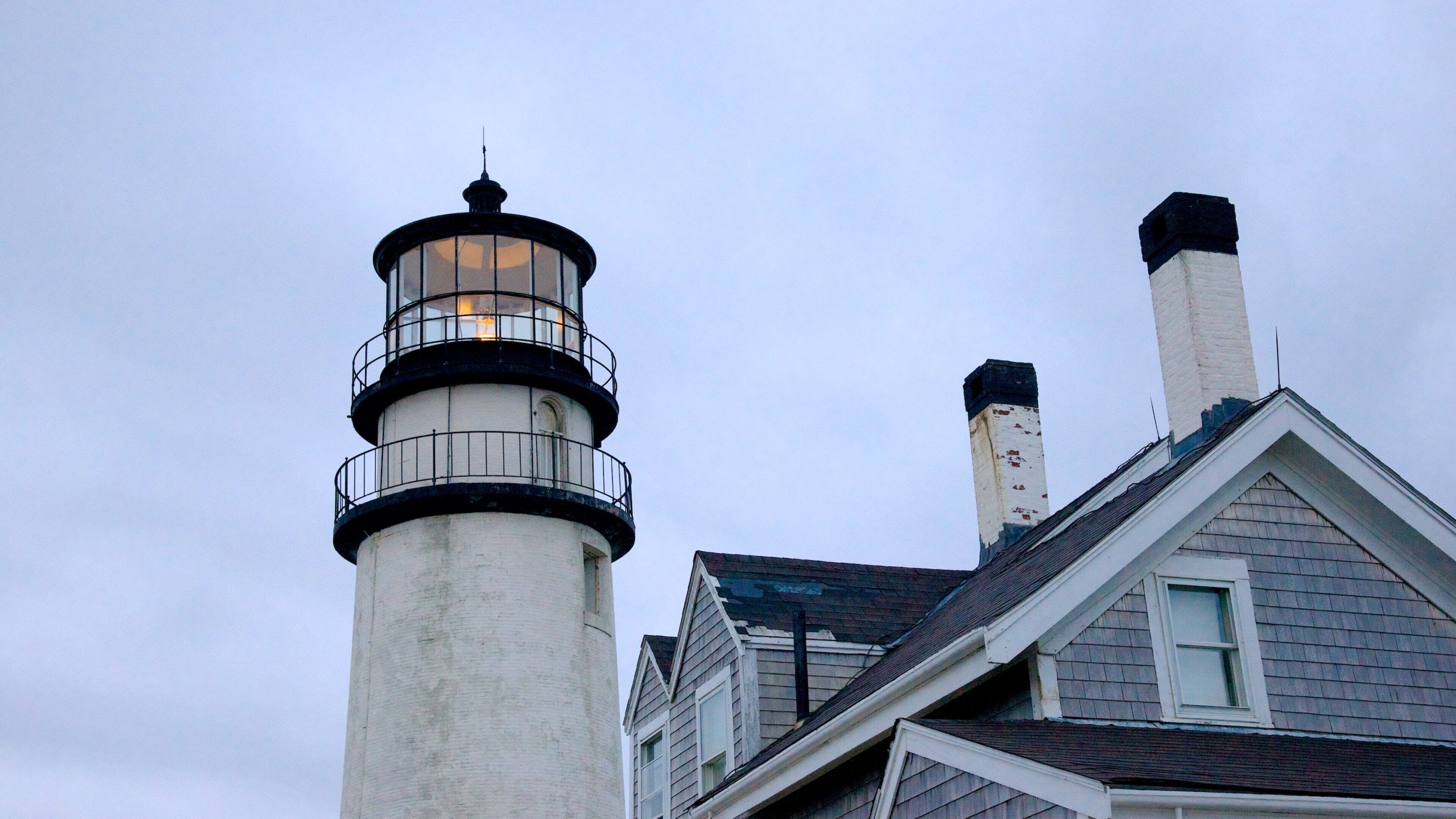 A lighthouse with a white tower and black top, next to a house with a gabled roof.