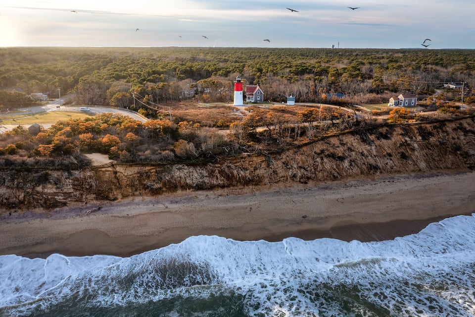 Un paisaje costero con un faro, una playa y colinas cubiertas de bosque.