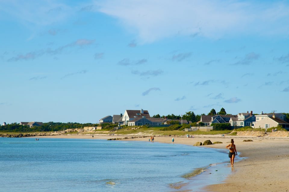 A beach with houses in the background and a person walking on the shore.