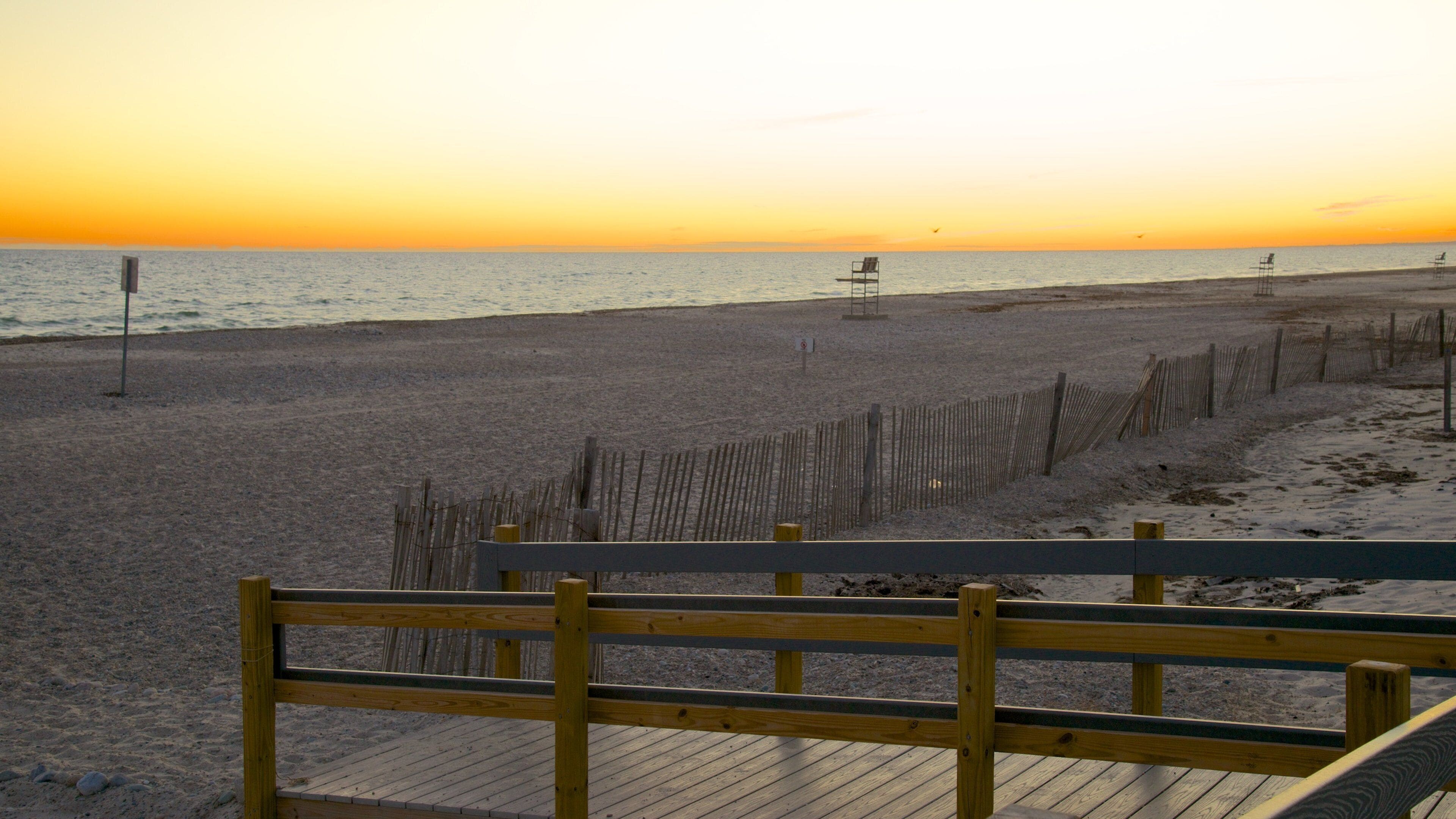 A beach at sunset with a wooden fence and a wooden walkway leading to the water.