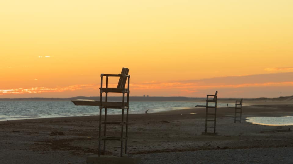 A beach with two empty chairs and a lifeguard stand at sunset.