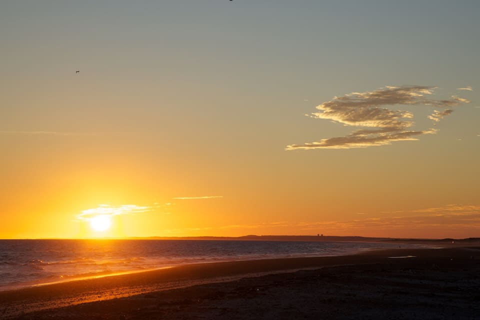 A sunset over a beach with the sun reflecting on the water.
