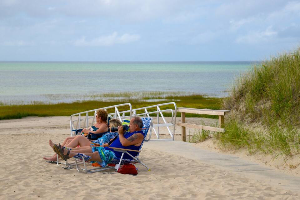 A beach with a wooden boardwalk and people relaxing on beach chairs.