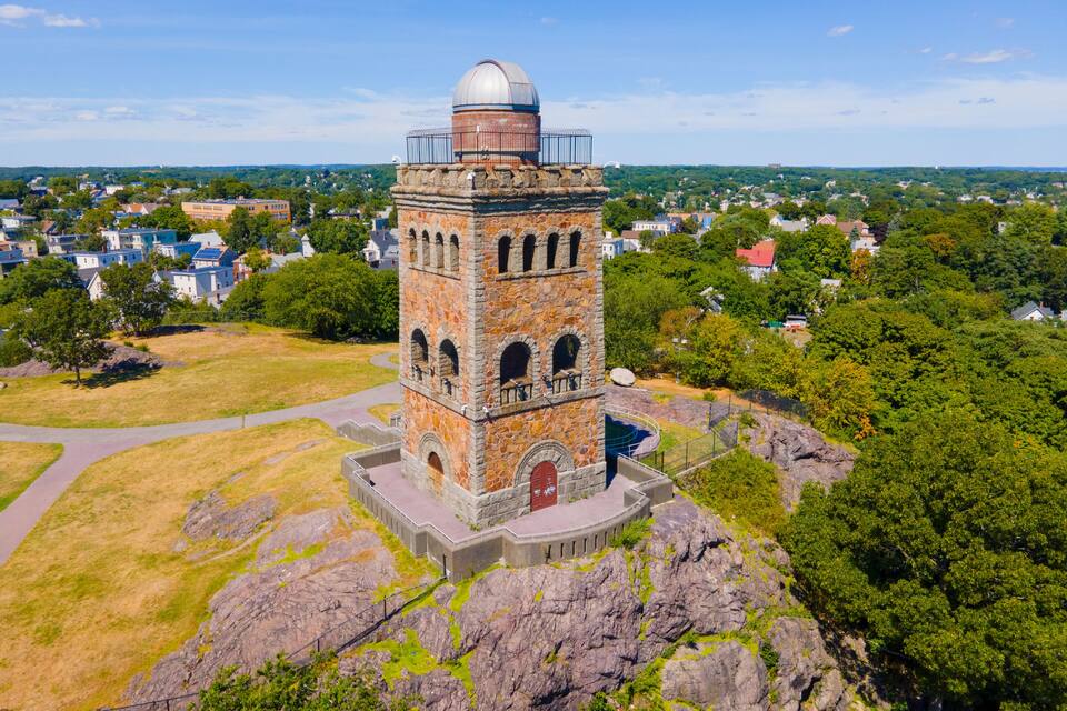 A stone observatory tower with a dome on top, surrounded by greenery and residential buildings.
