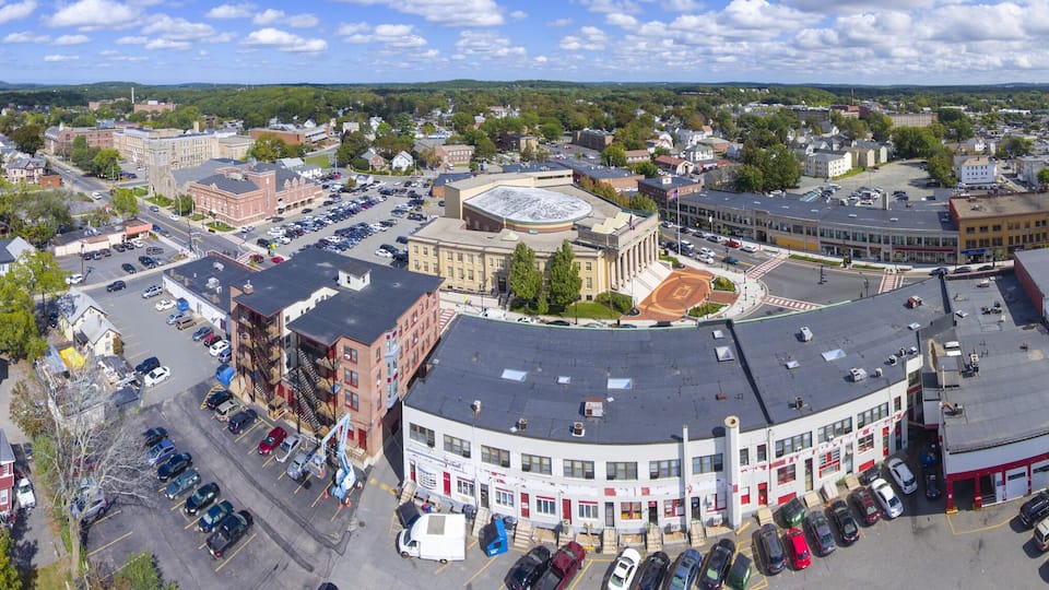 A panoramic view of a town with a central round building, surrounded by various buildings and a lake in the background.