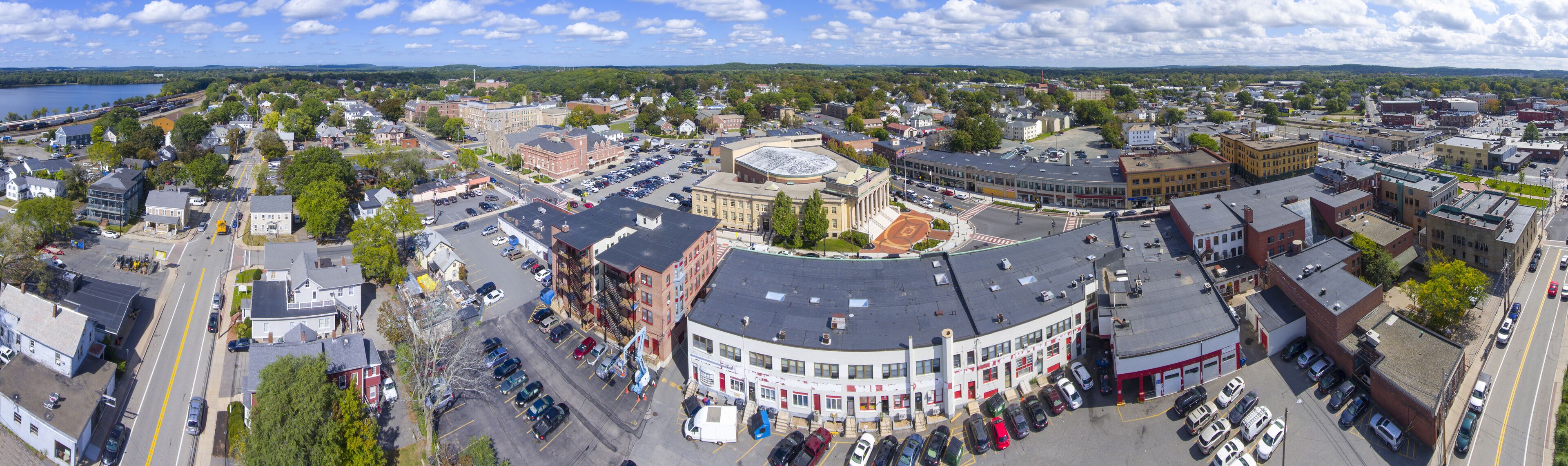 A panoramic view of a town with a central round building, surrounded by various buildings and a lake in the background.
