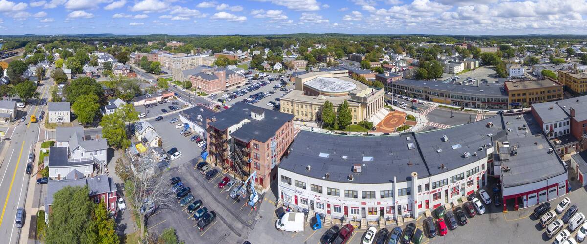 A panoramic view of a town with a central round building, surrounded by various buildings and a lake in the background.