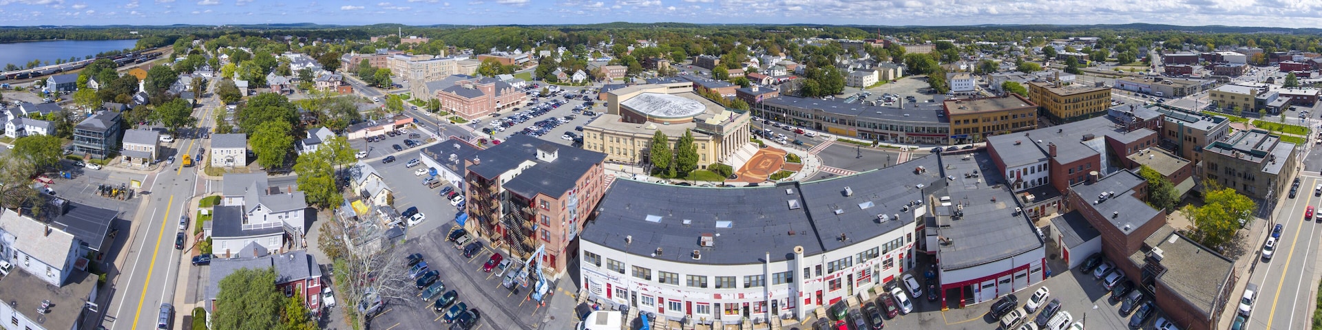 A panoramic view of a town with a central round building, surrounded by various buildings and a lake in the background.