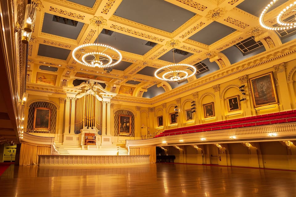 Interior de um teatro ornamentado com um órgão imponente, assentos vermelhos e decoração de teto elaborada.