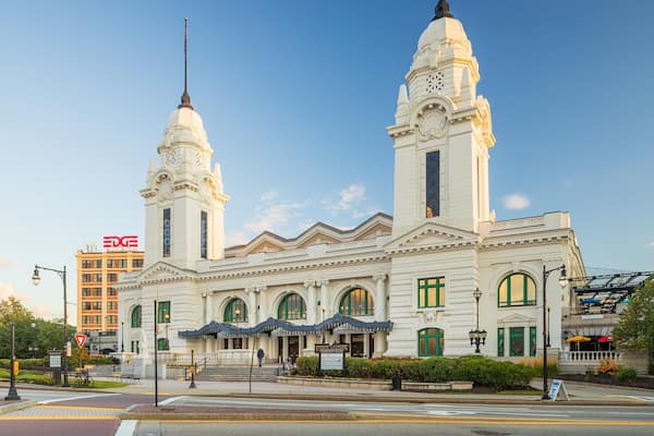 A historic white building with two towers and green windows, located at a city intersection.