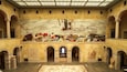 A grand hall with a large mural depicting a historical scene, arched columns, and a central statue.