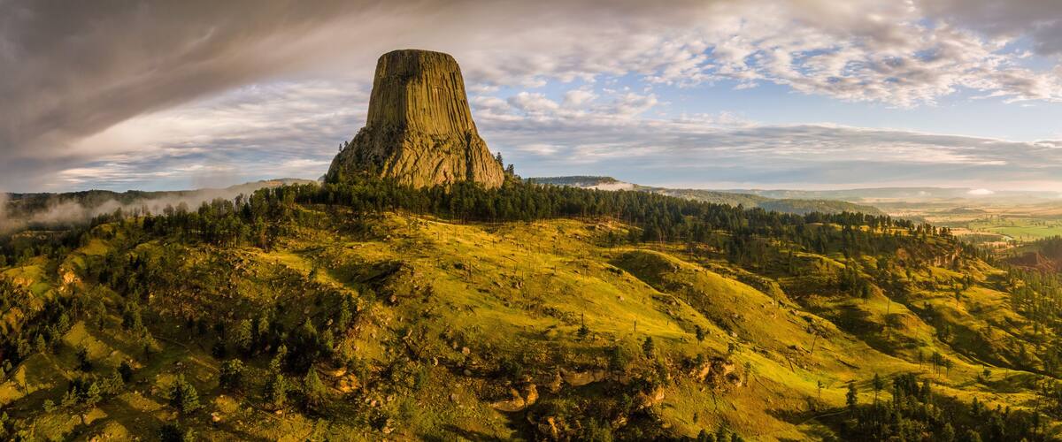 A large, steep rock formation surrounded by forested hills and a winding road.