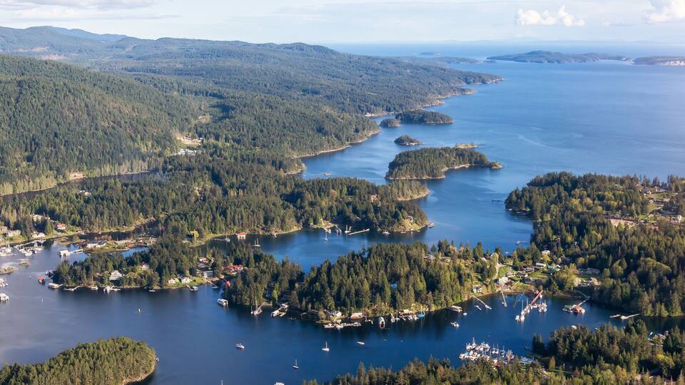 A coastal landscape with dense forests, a bay with boats, and distant islands.